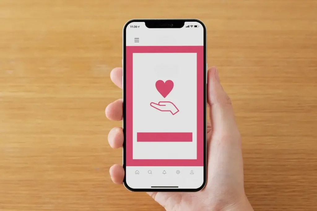 Mão segurando um smartphone com a tela exibindo um coração sobre uma mão aberta