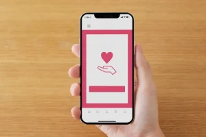 Mão segurando um smartphone com a tela exibindo um coração sobre uma mão aberta